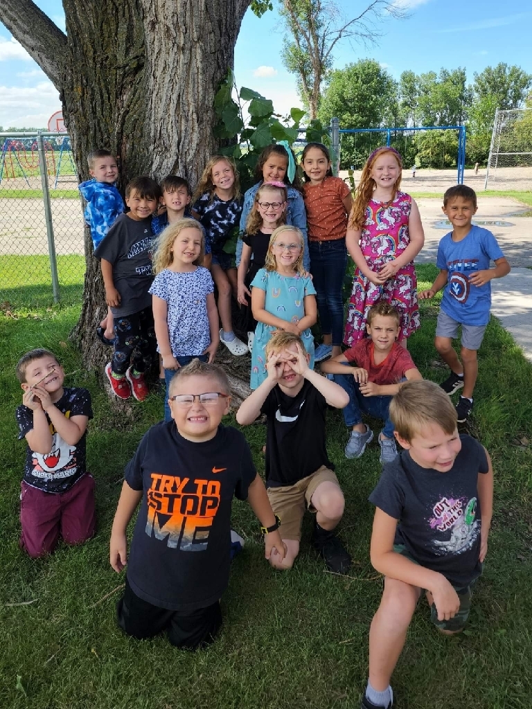 the first graders are posing in a group by the tree.