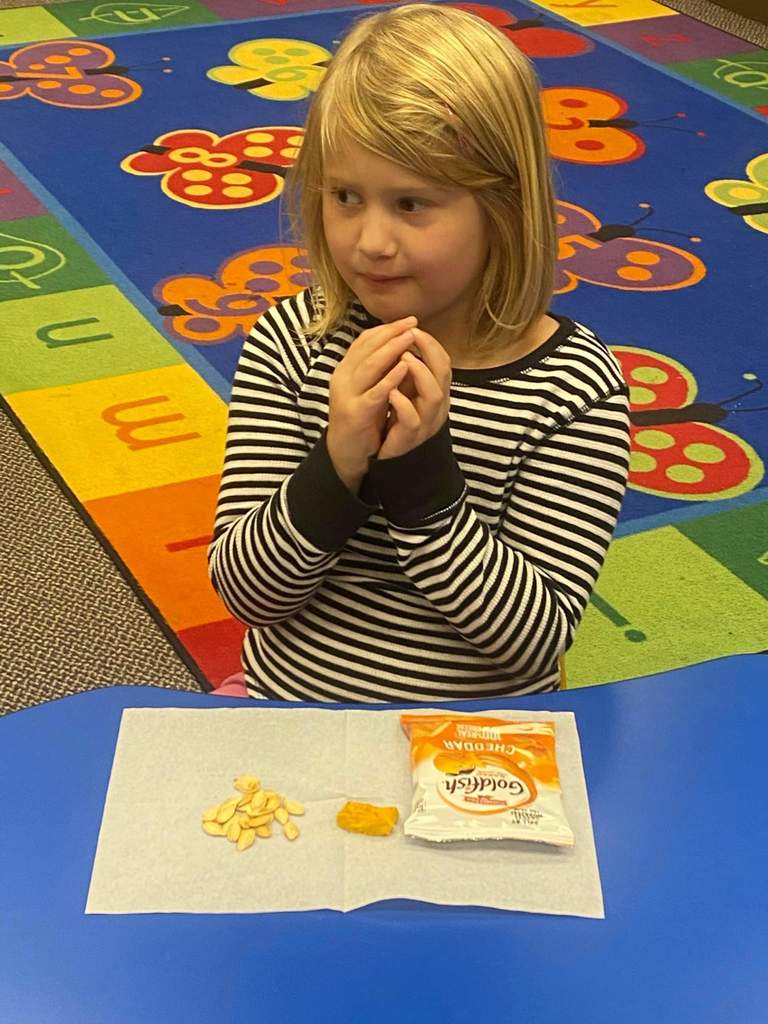 A girl tasting some seeds and pumpkin.