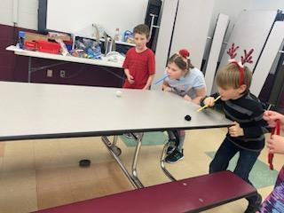 Kids blowing pompoms across the table.