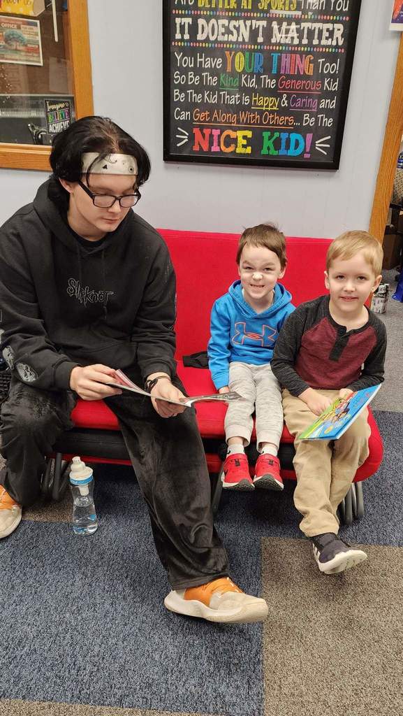 A boy reading a book to 2 kids.