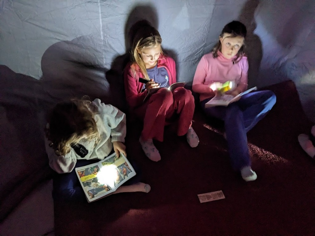 three girls reading in the tent with flashlights
